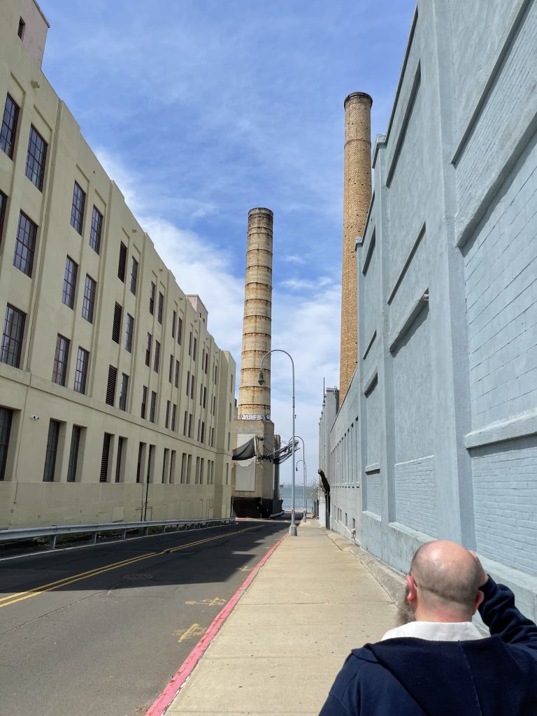 Photo of smoke stacks, building, and Kenny (in foreground)
